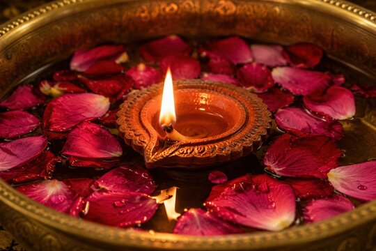 Traditional clay diya glowing among red rose petals during a festive Diwali celebration