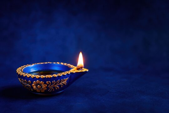 Ornate blue ceramic diya with bright flame against dark backdrop for Diwali celebration