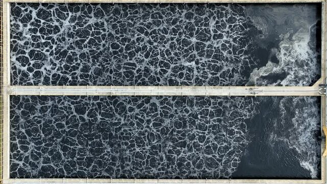 An aerial photography of industrial wastewater treatment ponds filled with dark water and oxygenation foam, highlighting environmental engineering, water recycling and sustainable resource management.
