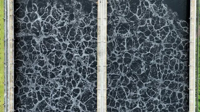 Drone perspective capturing black wastewater in industrial treatment tanks with active aeration surfaces, representing wastewater processing, industrial pollution reduction and clean water technology.