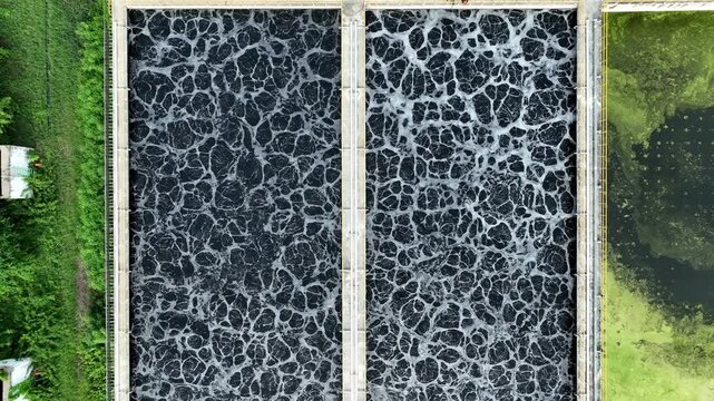Aerial view of dark industrial wastewater treatment basins with foamy aeration patterns, showcasing water purification processes, pollution control, and sustainable environmental management systems.
