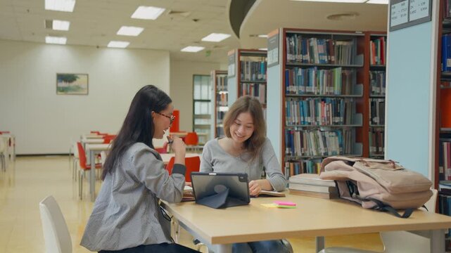 Asian and Caucasian female students study together in university library.