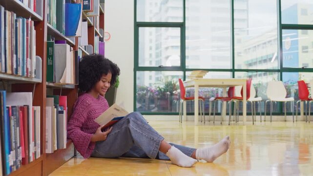 African American young girl sit on floor and reading books in library. 