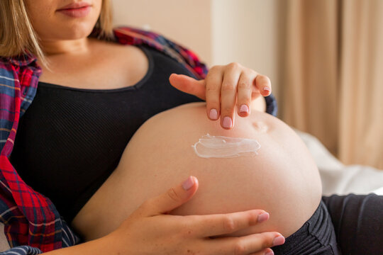 Pregnant woman applying cream to exposed belly for prenatal skincare and belly care comfort