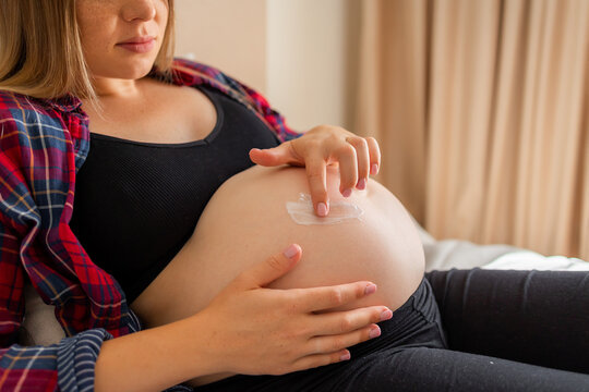 Expectant mother applying moisturizer to baby bump at home in a relaxed maternity moment