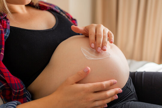 Pregnant woman applying cream to her bare belly in a relaxed maternity skincare moment