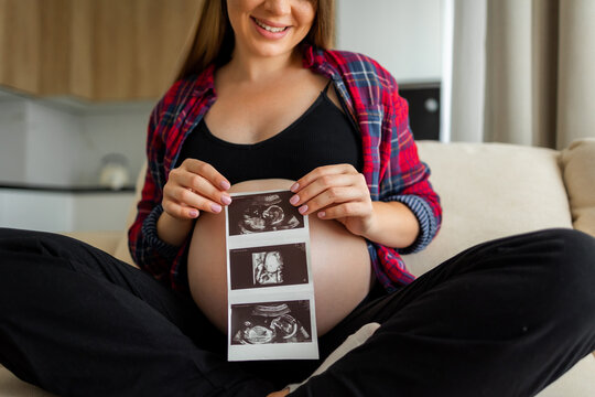 Pregnant woman with big belly preparing for the arriving of a newborn. Expecting female on a third trimester with ultrasound image of child.