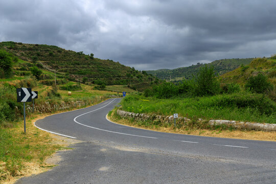 A scenic asphalt road curves through lush agricultural land with verdant lawns and hills, hinting at a recent harvest season
