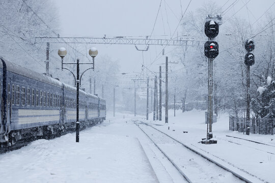 Snowy train station with passenger train and traffic signals in winter weather
