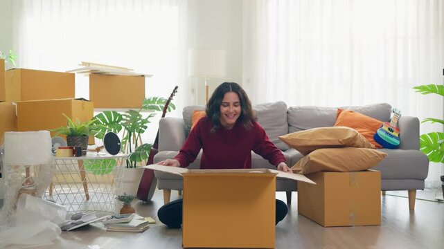 Young Hispanic woman arranging furniture and unpacking boxes in house.