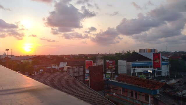 Cilacap, Indonesia - April, 27, 2021: High angle rooftop view of an urban cityscape during a golden hour sunset. Dramatic orange and purple clouds spread across the evening sky with the bright sun set