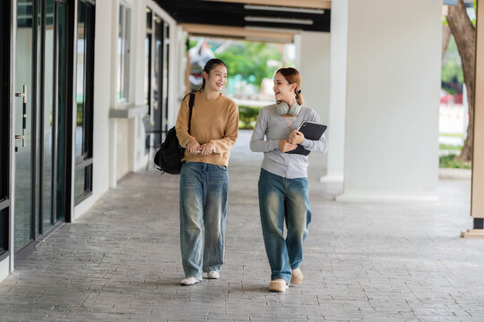 Two Young Asian Female College Students Walking and Talking Together on University Campus