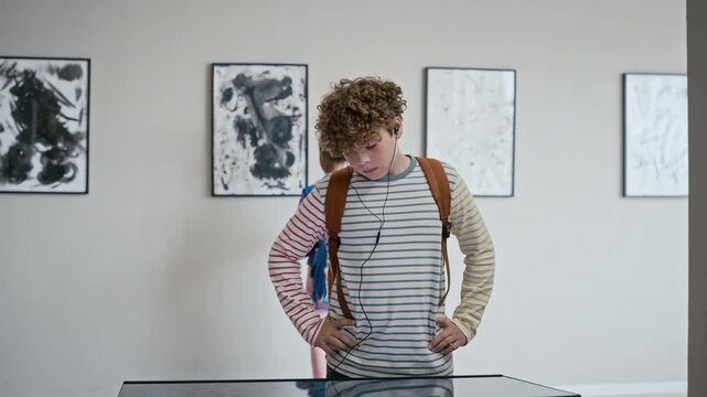 African American teenage girl and Caucasian teenage boy wearing earphones looking at exhibits in modern art gallery. Footage is ideal for educational programs and museum promotion