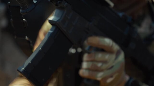 Extreme close-up of soldier's hands in camouflage tactical gloves inserting magazine into assault rifle and reloading weapon in combat. Military warfare concept for defense, armed forces and editorial