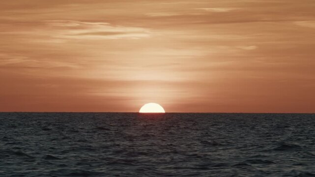 Sunset in the open sea. Sun hides in the sea as seen from the moving sailing vessel.
