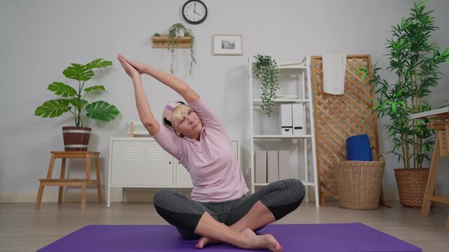 Caucasian senior woman practicing yoga pose on mat in living room at home.