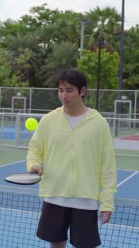 Young male pickleball player balancing a pickleball on paddle on outdoor court. 