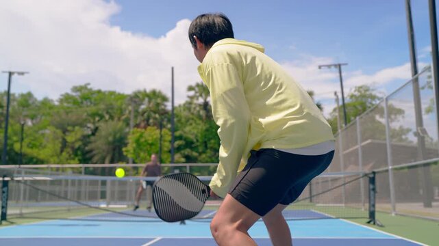 Young man and woman playing mixed doubles pickleball on outdoor court. 