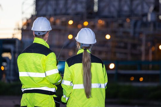 Oil refinery engineers team inspecting industrial plant at night twilight, Petroleum plant workers in safety gear looking at facility in evening, Energy industry professionals checking site