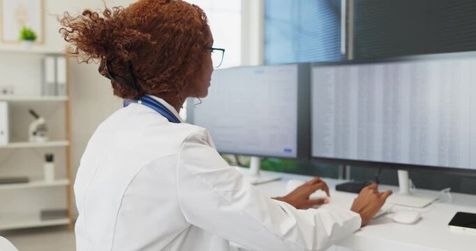 Doctor physician woman at computer in clinic. Reviewing records for healthcare analysis on dual monitors at a workstation, organizing data for diagnostics. Clear data flow in modern medicine.