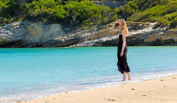 Tranquil woman with flowing curly hair enjoys a serene moment by the turquoise sea