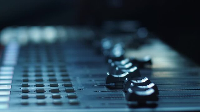 Close-up of a professional sound mixing console in a recording studio with illuminated buttons and controls. Audio engineer presses buttons to adjust channels for music production, broadcasting,