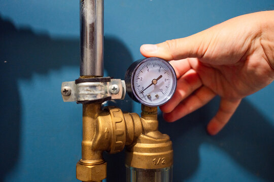 Hand showing zero pressure on pressure gauge on water pipe with blue wall background