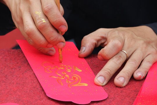 Close-up of a calligrapher hands writing traditional greetings with gold paint on a red envelope for Tet Lunar New Year, Ho Chi Minh City, Vietnam.