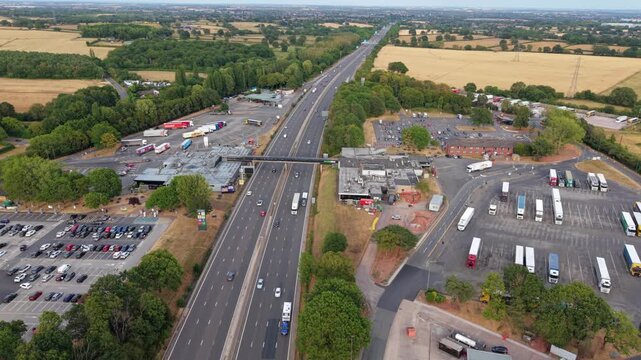 Aerial orbit view of busy motorway service station and traffic slip roads on M6 in Warwickshire UK