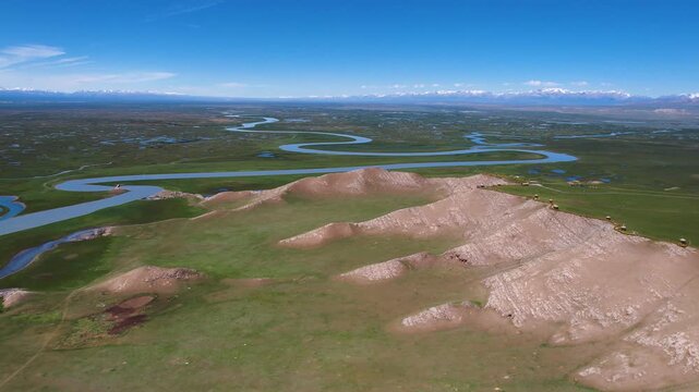 Aerial view of winding river across open plain with hills and distant mountains