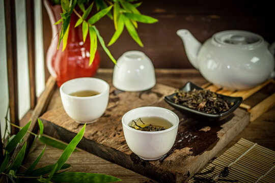 Traditional Asian Oolong tea served in white ceramic cups on an antique wooden table with loose leaves and bamboo, creating a peaceful and refined atmosphere for health wellness and relaxation.