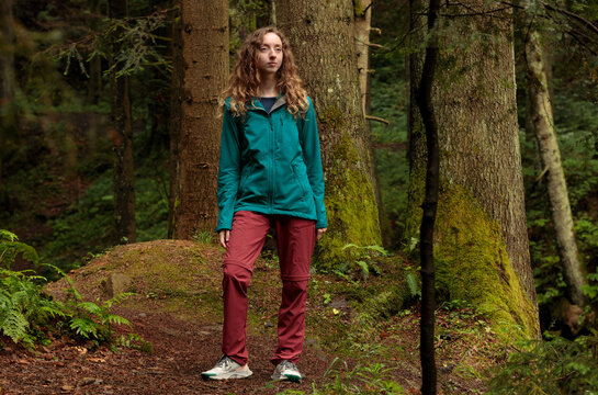 Young woman in hiking clothes stands in a lush green forest surrounded by trees lifestyle advertising concept for posters