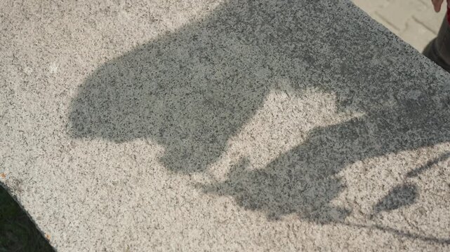 Close up of textured concrete surface with shadows cast by unseen object showing subtle variations in color and pattern. scene is outdoors on bright daylight revealing rough grain detail