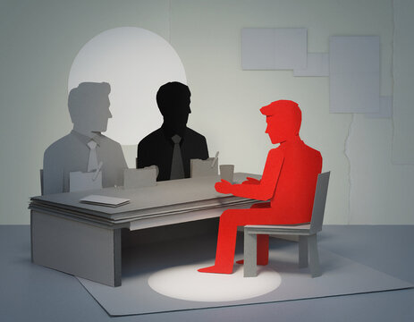 A job interview scene constructed from cut paper, featuring a spotlit red figure sitting opposite grey and black silhouette interviewers.