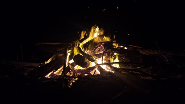 Bright bonfire burning with glowing sparks and flames on wood logs in the dark night outdoors