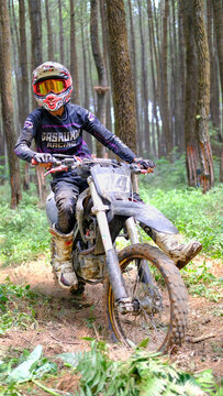 MALANG, INDONESIA - AUGUST 23, 2026: Motocross rider on a dirt bike in a pine forest, navigating an off-road trail for adventure sport.