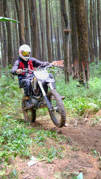 MALANG, INDONESIA - AUGUST 23, 2026: Motocross rider on dirt bike in protective gear jumping on a forest trail
