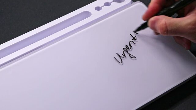 European male hand writing urgent on whiteboard with black pen and erases it with white sponge afterwards for seamless looping message writing on whiteboard. ASAP very urgent text