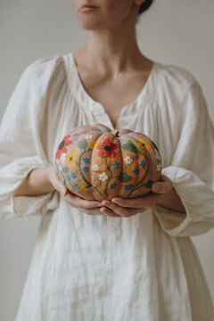 Woman In White Dress Holding Hand Painted Floral Pumpkin With Both Hands