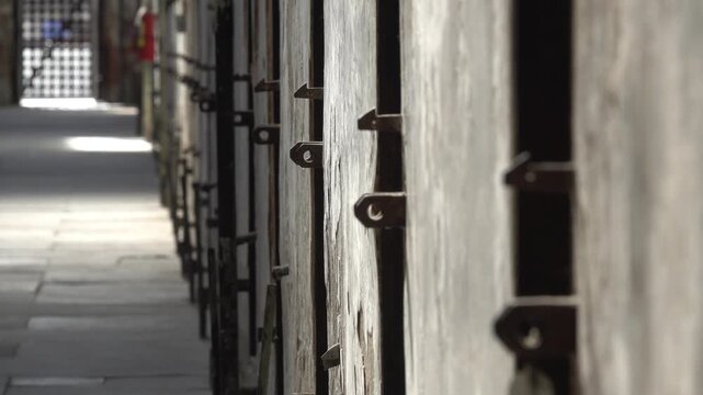 Row of prison cells with metal doors and locks, historical architecture and confinement footage.