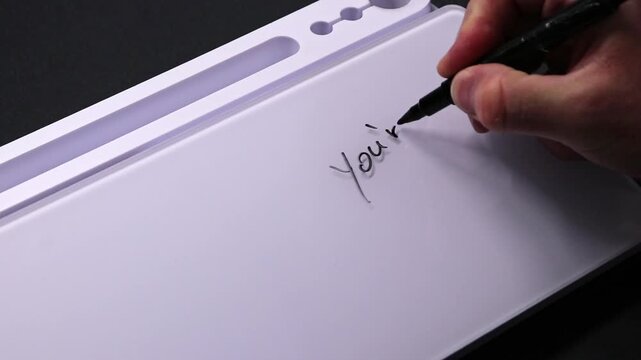 European male hand writing you&acute;re doing awesome on whiteboard with black pen and erases it with white sponge afterwards for seamless looping message writing on whiteboard. Positive feedback on support