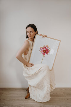 Young Female Artist Posing With Framed Flower Picture Sitting On Wooden Stool