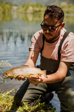 Fisherman holds a brown trout by the lake during summer