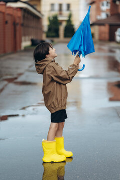 A smiling boy holds a blue umbrella in a wet street puddle