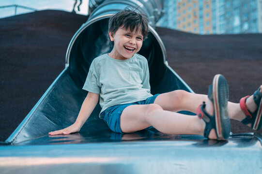 Happy boy rides a metal slide at the outdoor playground
