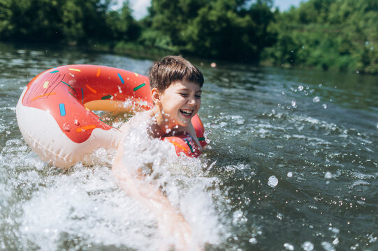 A happy boy splashes water while swimming with an inflatable ring