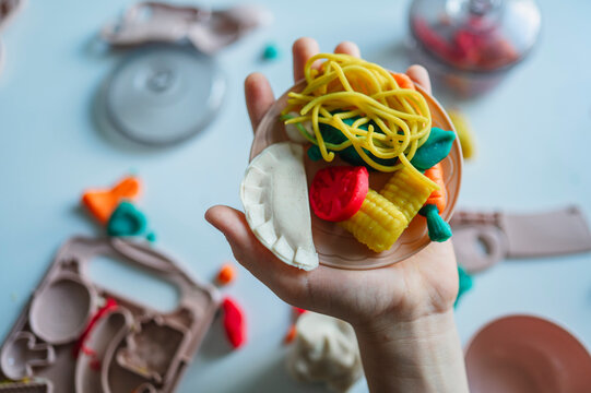 Boy holds a toy plate with colorful playdough food at home