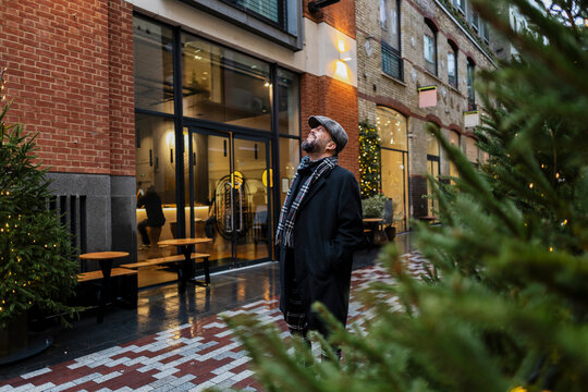Man in coat and flat cap looks up at outdoor festive winter market