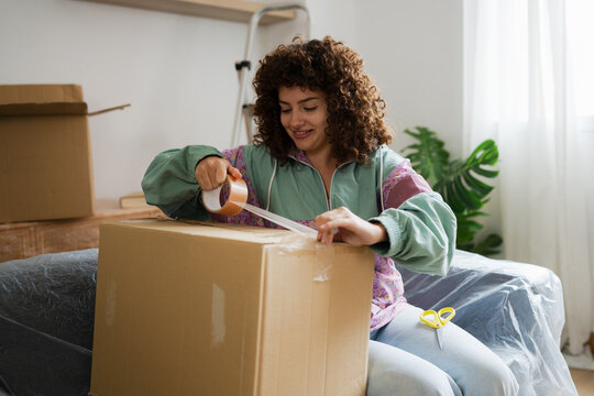 Smiling woman taping cardboard box while packing for moving at home