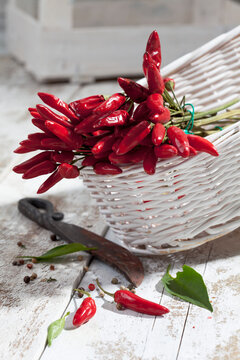 Red chili peppers (Capsicum) in white basket on white wooden table, studio shot